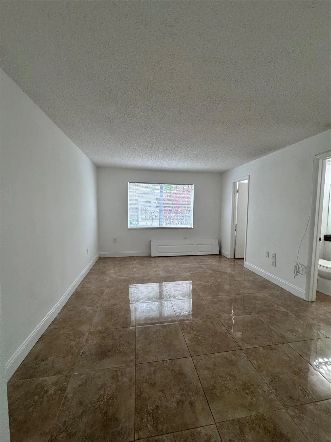 Glossy large-format tile flooring, window with blinds, and white painted walls