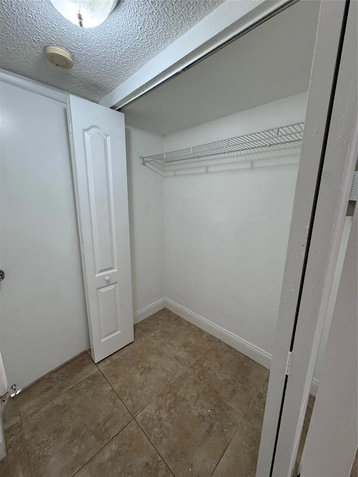 Walk-in closet featuring built-in wire shelving, ceramic tile flooring, and white bifold doors