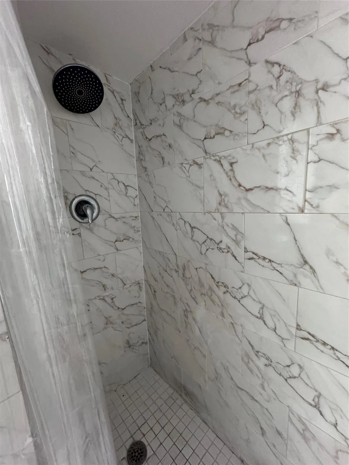 Shower featuring large format wall tiling, a rainfall showerhead, and a tiled floor