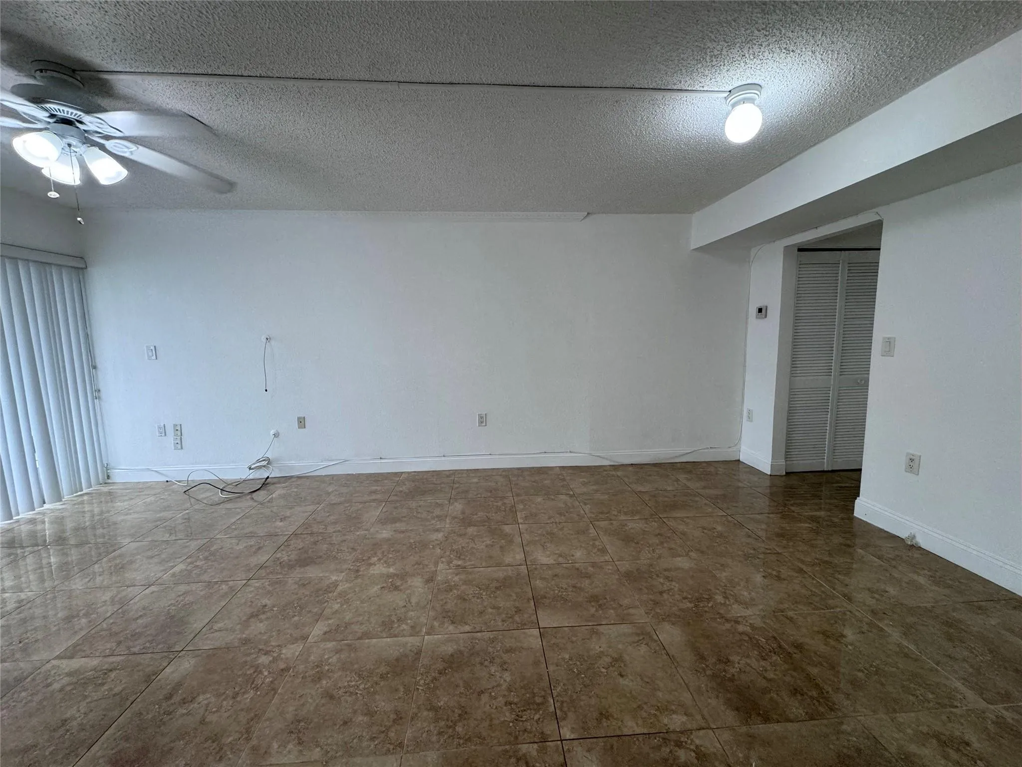 Expansive room with large format tile flooring, a ceiling fan, and a built-in closet with louvered bifold doors