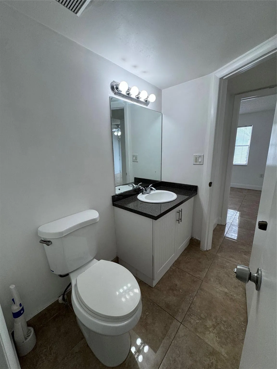 White vanity cabinet with a dark countertop, undermount sink, and wall-mounted mirror with overhead lighting