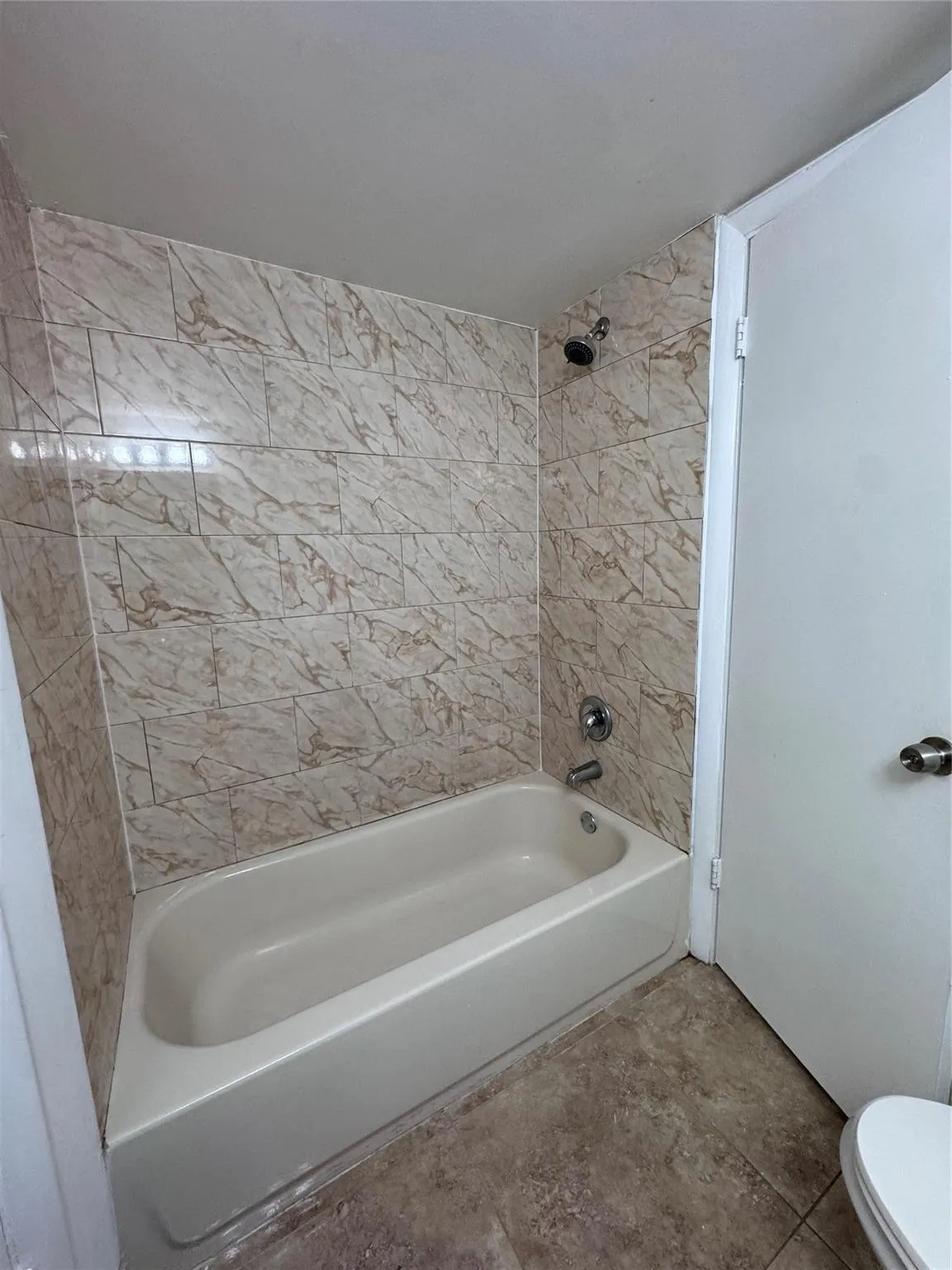 Bathtub and shower combination featuring tiled surround, chrome fixtures, and tiled flooring