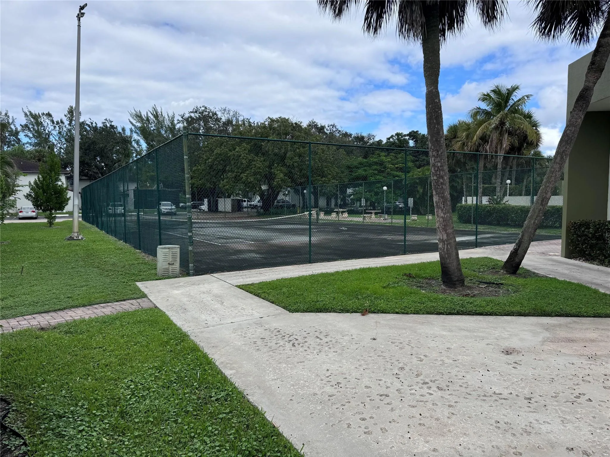 Tennis court with chain-link fencing, surrounded by mature trees and manicured lawn