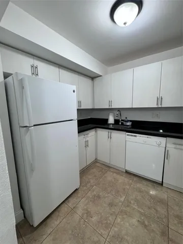 Kitchen featuring white cabinetry, dark countertops, a white refrigerator, a white dishwasher, and tile flooring