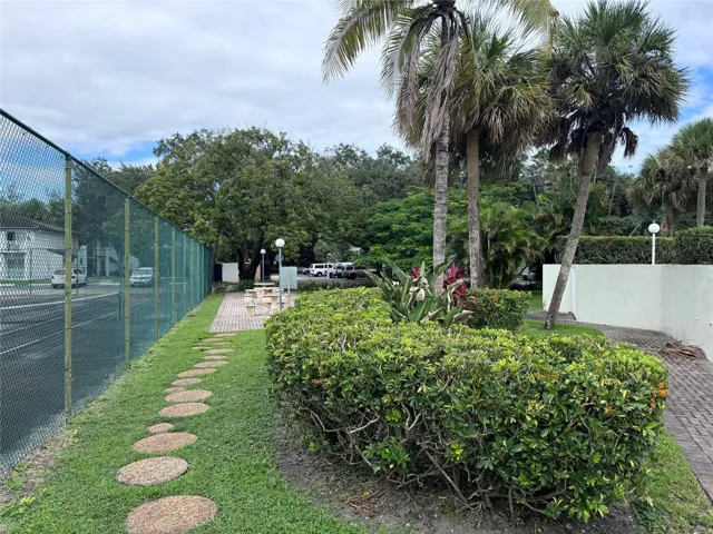 Outdoor amenity area featuring mature palm trees, established landscaping, and a patio with a picnic table