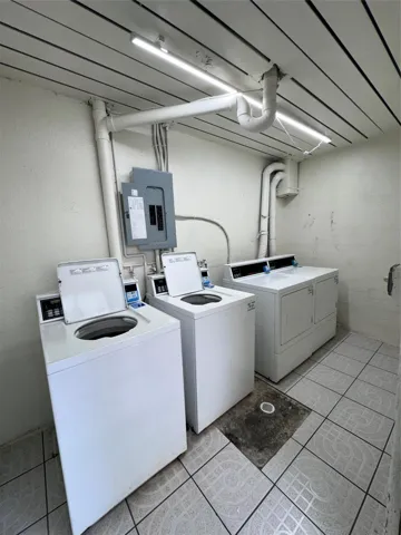Tiled flooring, exposed overhead piping, flush-mount ceiling lighting, and a visible electrical panel