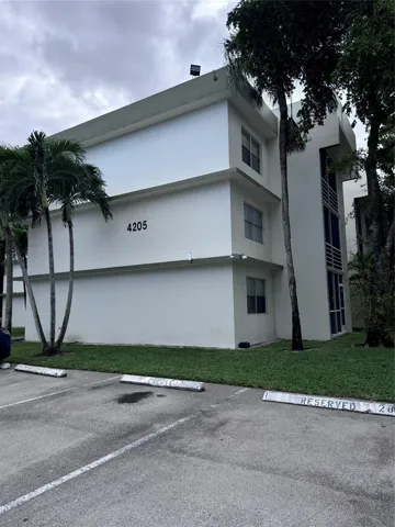 Multi-story building featuring a flat roofline, perimeter landscaping, and an adjacent asphalt parking area with marked spaces
