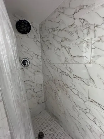 Shower featuring large format wall tiling, a rainfall showerhead, and a tiled floor