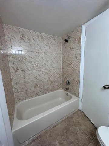 Bathtub and shower combination featuring tiled surround, chrome fixtures, and tiled flooring