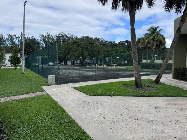 Tennis court with chain-link fencing, surrounded by mature trees and manicured lawn