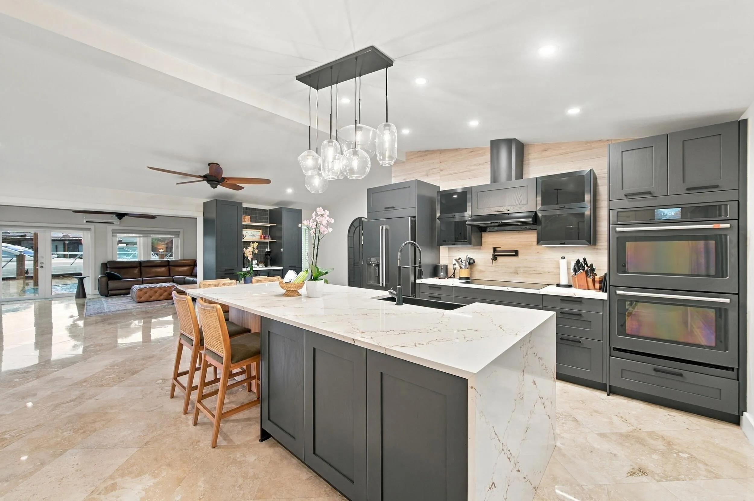 Kitchen featuring a waterfall-edge island with seating, a pendant light fixture, dark cabinetry, and dual built-in ovens