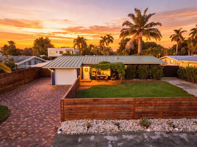 Metal roof, attached garage, brick paver driveway, wood privacy fence, and mature landscaping