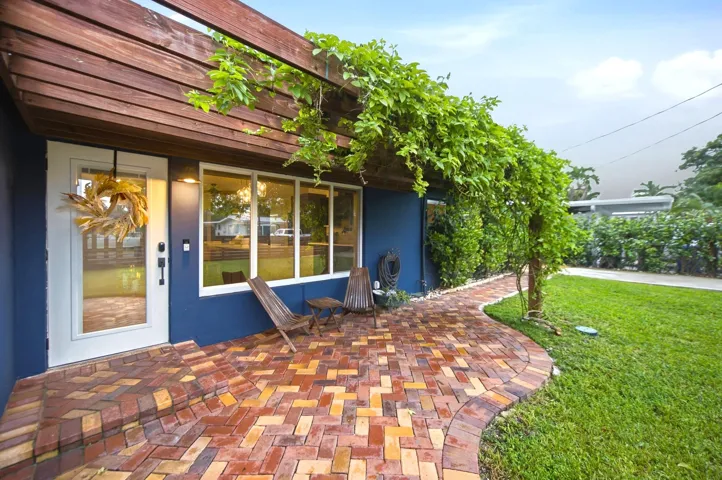Wood pergola with lush greenery over a brick paver patio, featuring a full-light entry door and multiple windows