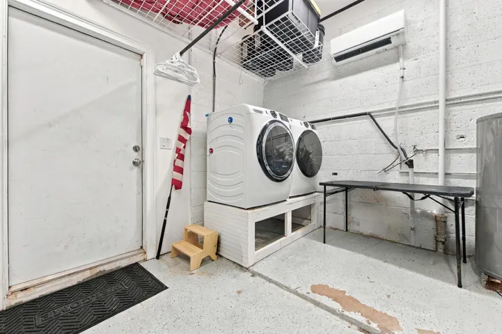 White front-loading washer and dryer, exposed concrete block walls, and overhead shelving
