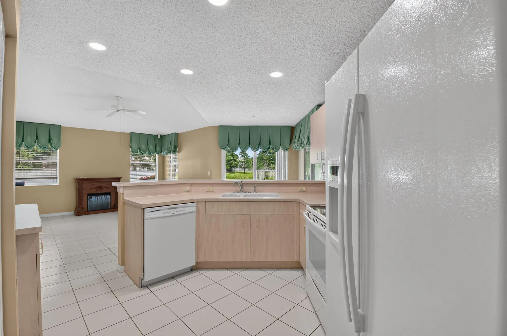 Kitchen featuring light wood-finish cabinetry, white appliances, and a pass-through counter to the family room
