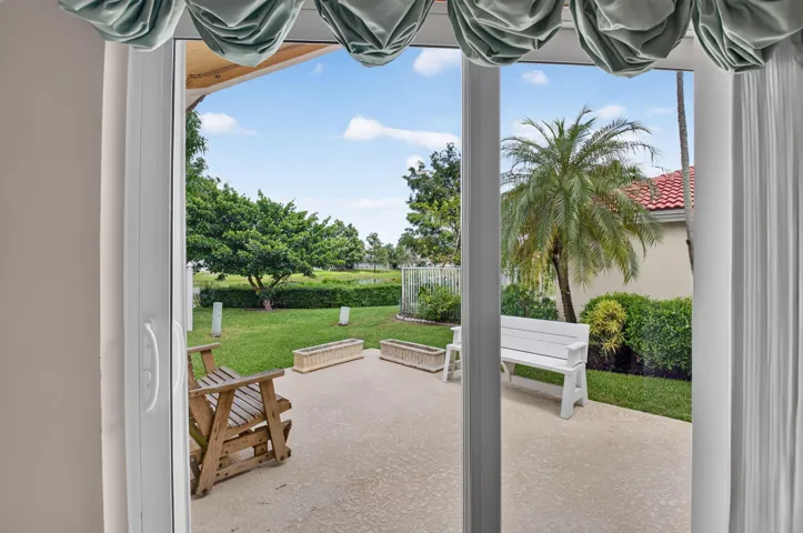 Sliding glass doors opening to a patio with water views, grassy yard, and mature landscaping