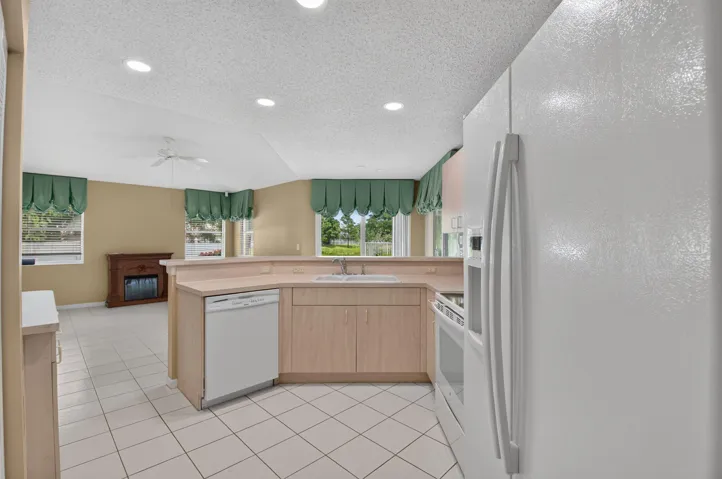 Kitchen featuring light wood-finish cabinetry, white appliances, and a pass-through counter to the family room