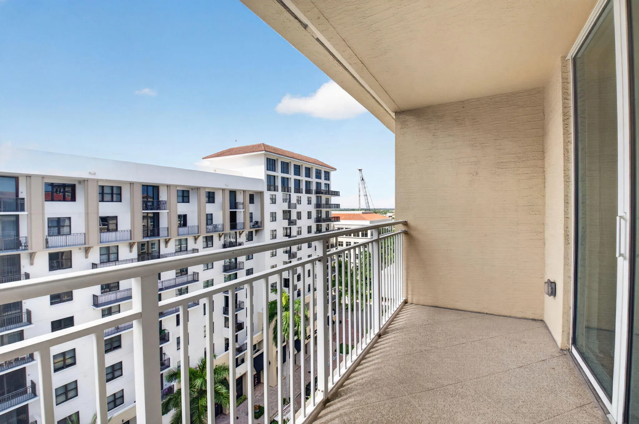 Private balcony with textured concrete flooring, white metal railing, and sliding glass door access