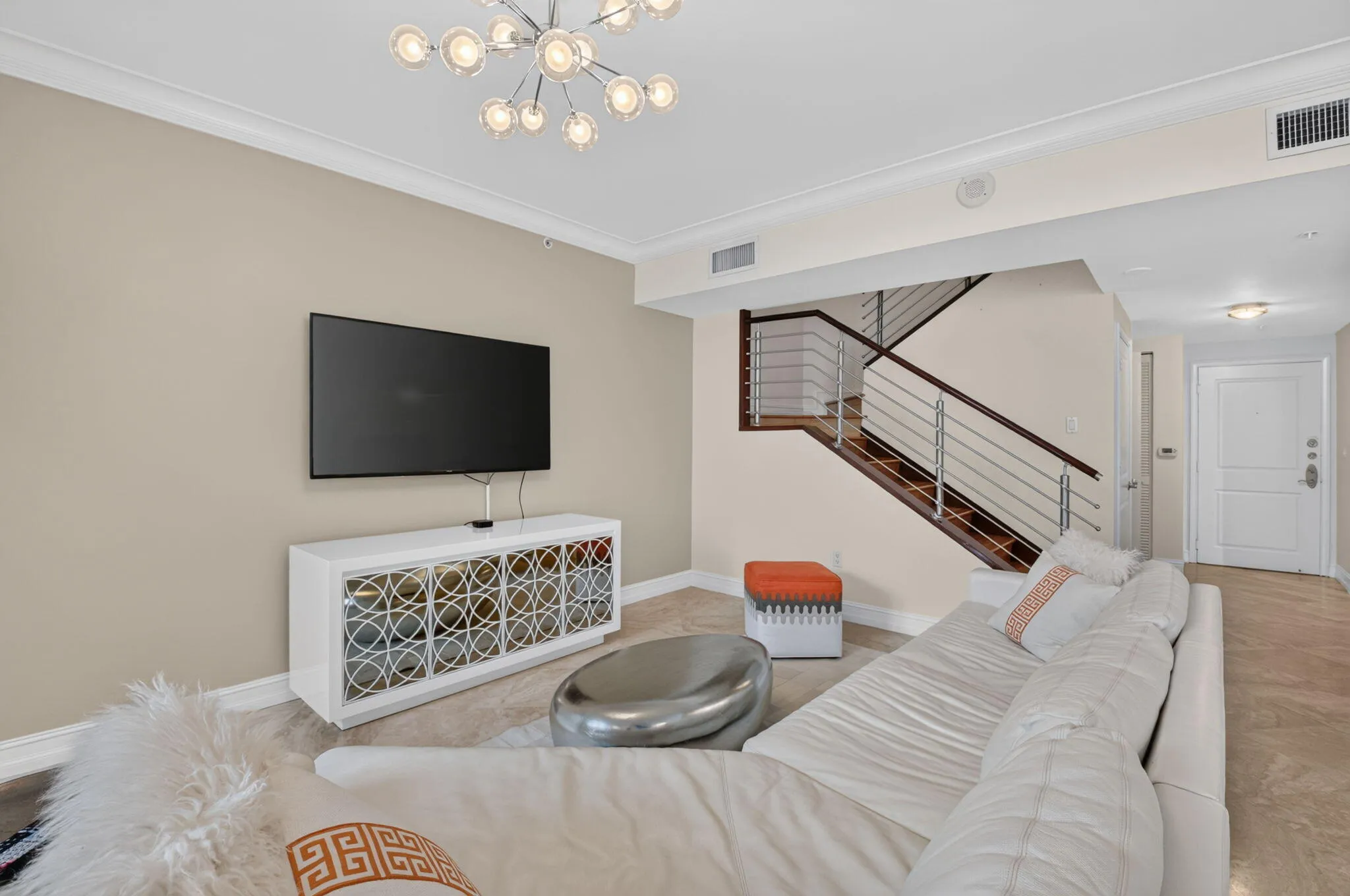 Modern chandelier, crown molding, wall-mounted television, built-in media console, and wood-finish staircase with metal railings