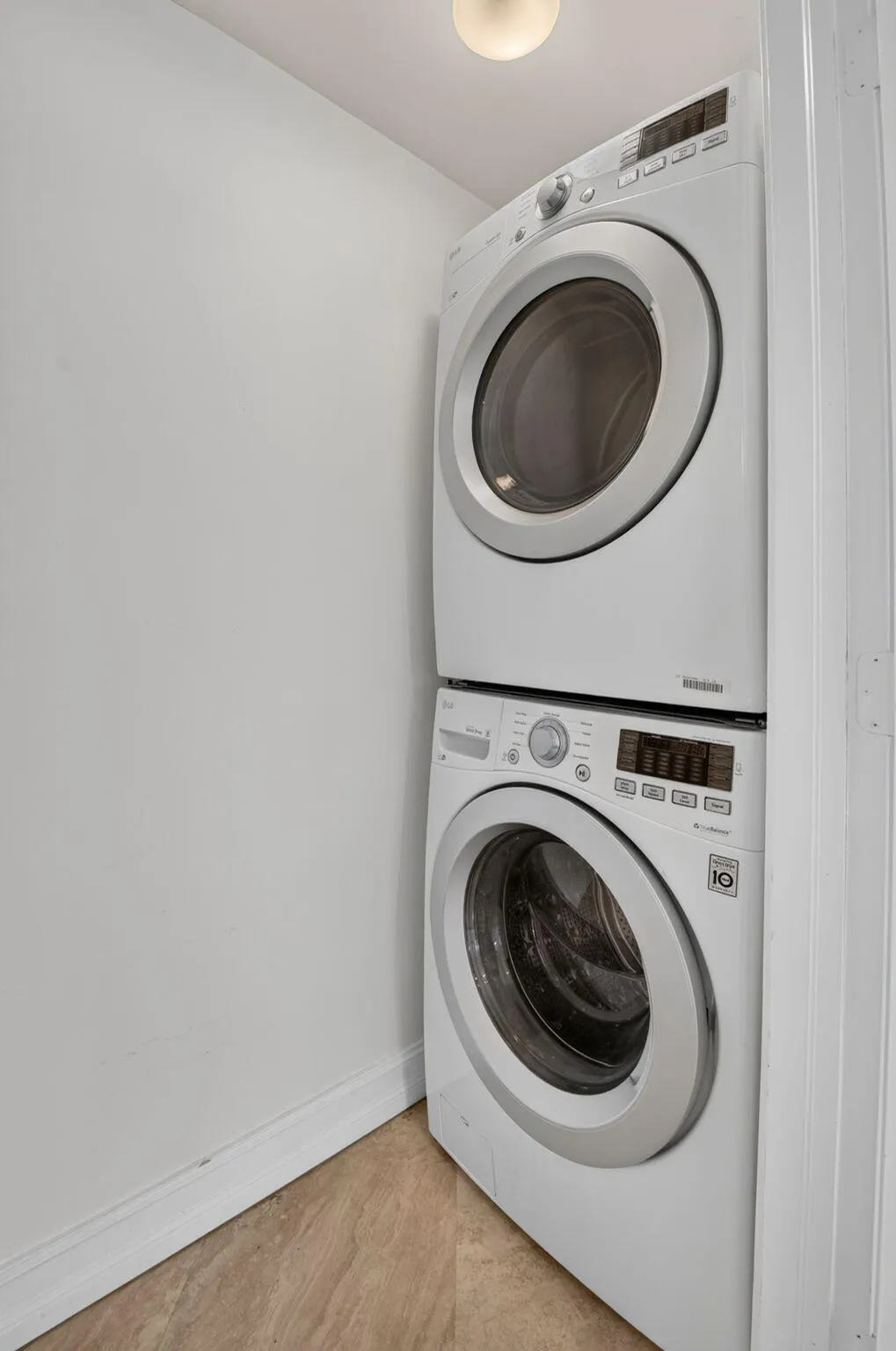 Stackable washer and dryer unit with a light fixture and wood-finish flooring