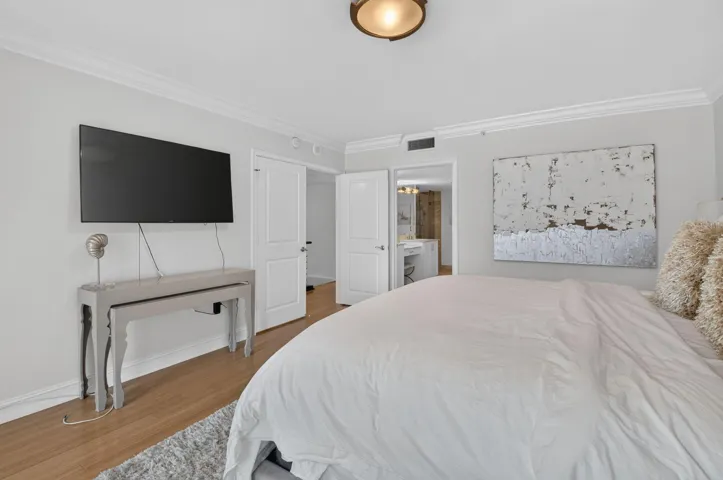 Crown molding with a light fixture, wood-finish flooring, and a white paneled door