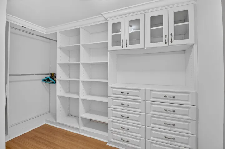 Custom closet organization system featuring white cabinetry, glass-front upper cabinets, multiple drawers with hardware, open shelving, and a hanging rod