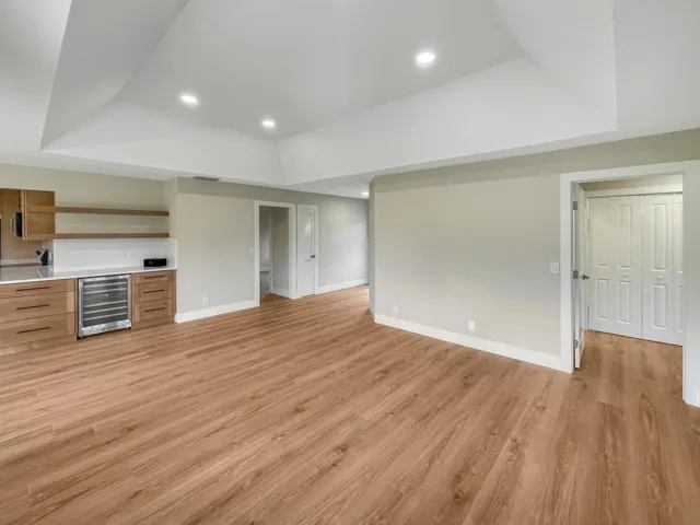 Spacious room featuring wood-finish flooring, recessed lighting, and a built-in wet bar with wood cabinetry, a beverage refrigerator, and open shelving