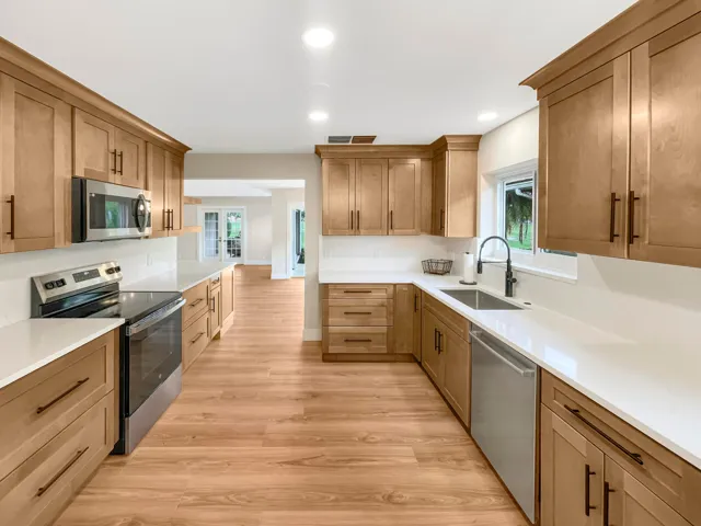 Light wood-finish cabinetry with dark hardware, white countertops, and stainless steel appliances
