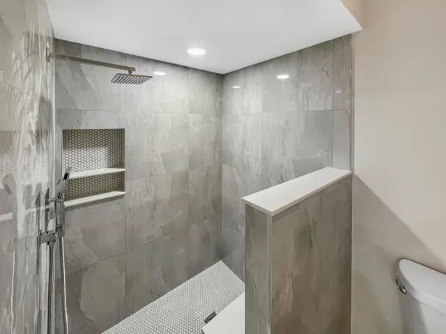 Tiled shower with a rain shower head, hand-held sprayer, built-in shelving, and a mosaic tile floor