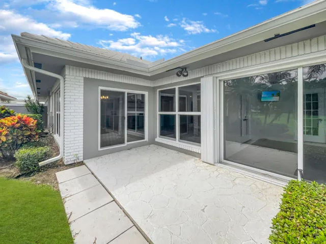 Exterior with white brick accent, gray stucco finish, multiple sliding glass doors, white window frames, and a textured concrete patio
