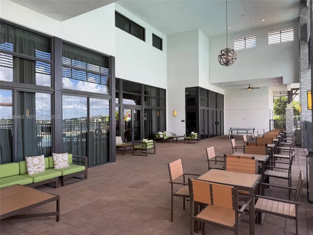 Covered outdoor patio featuring paver flooring, expansive floor-to-ceiling glass panel walls, dual-story ceiling height, and hanging spherical pendant lighting