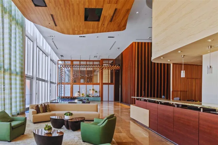 Floor-to-ceiling windows, wood-finish ceiling, wood-slat accent wall, polished stone flooring, and a built-in reception desk