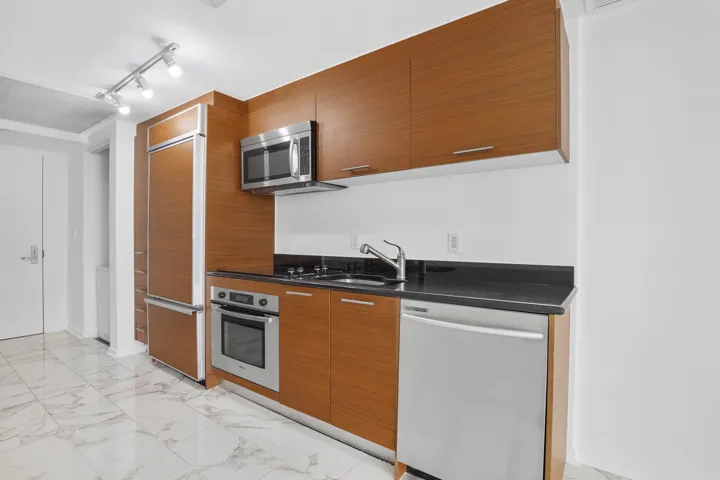 Featuring wood-finish cabinetry, stainless steel appliances, black countertops, and a subway tile backsplash. Cook here, then walk ten feet to the sliders. Come see the layout; photos compress the run.