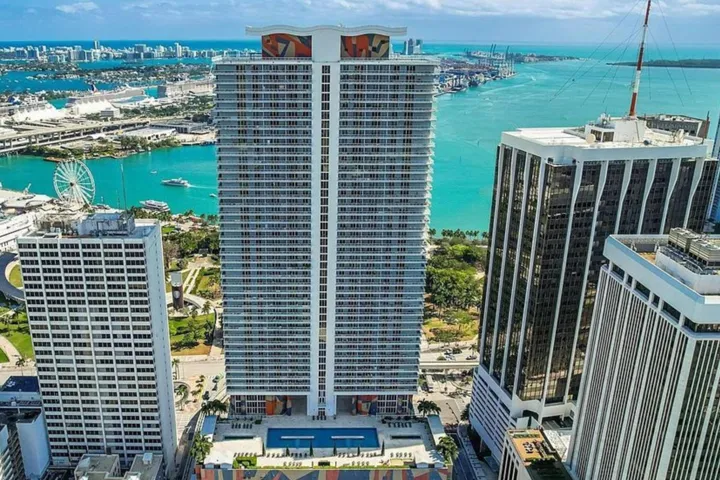 Contemporary high-rise building with extensive balconies, a rooftop pool, and surrounding urban architecture
