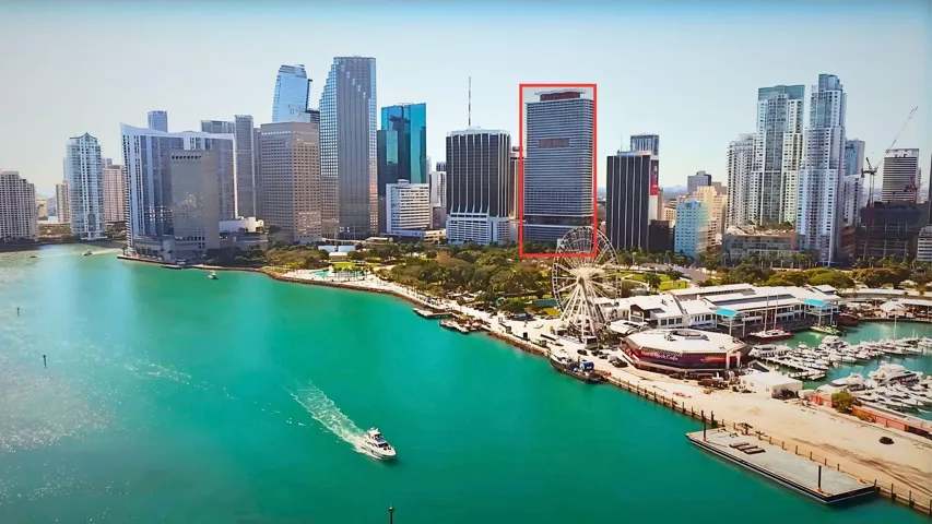 High-rise building with a flat roofline, surrounded by a dense urban skyline, waterfront setting, adjacent to a marina, and a Ferris wheel
