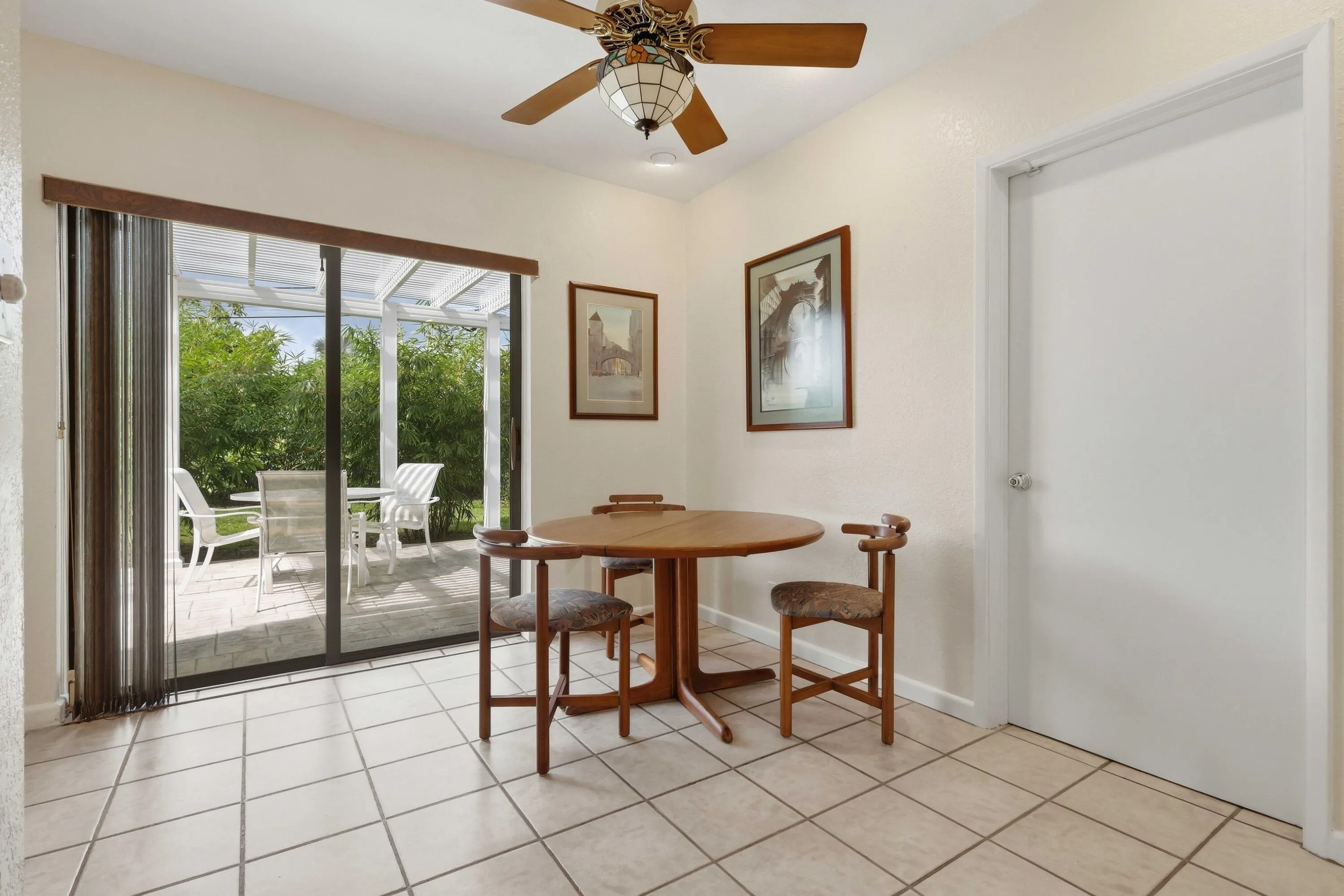 Light-toned tile flooring, sliding glass door with vertical blinds, outdoor patio featuring a white pergola, and a ceiling fan with integrated lighting