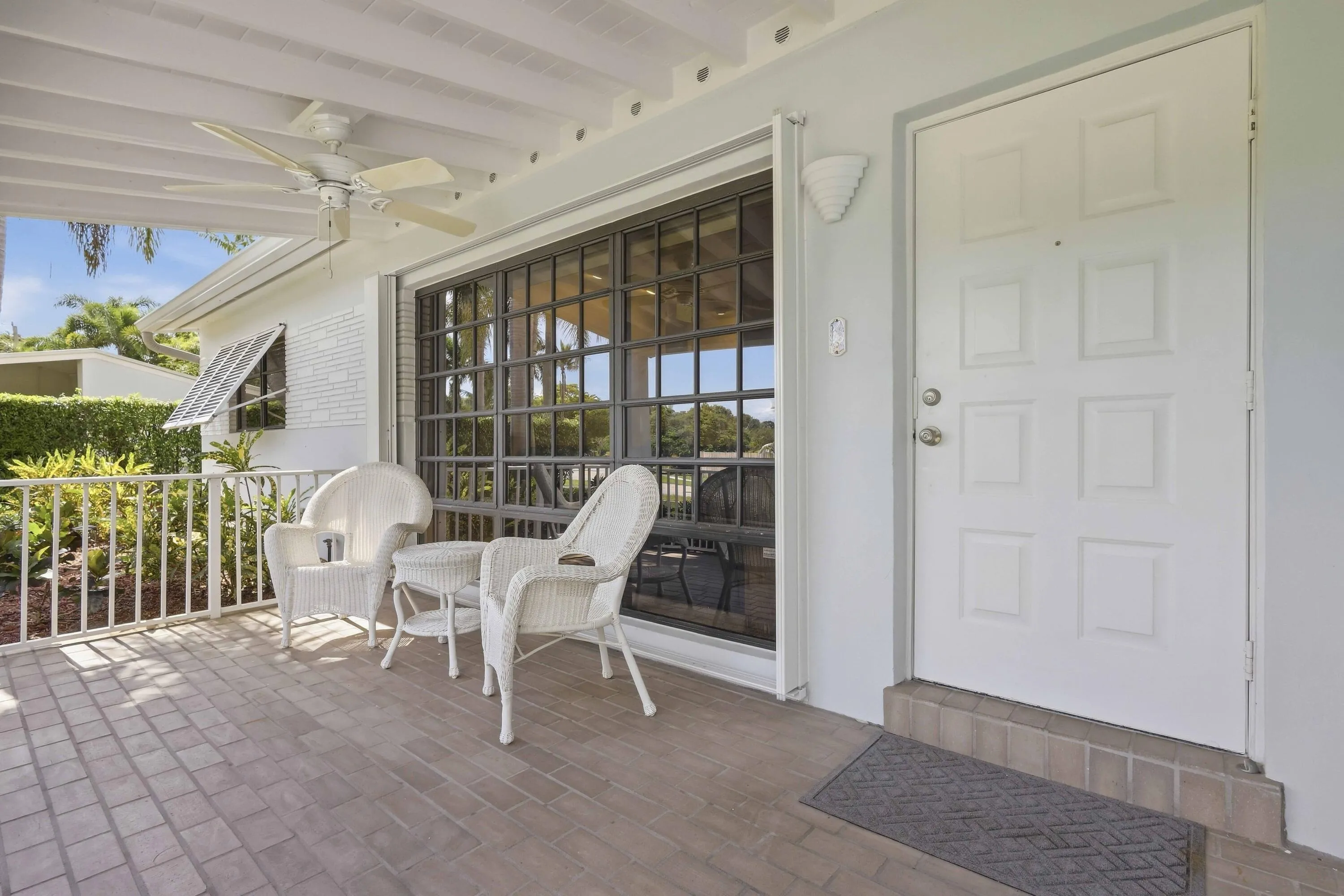 Covered porch with textured paver flooring, white railing, and ceiling fan