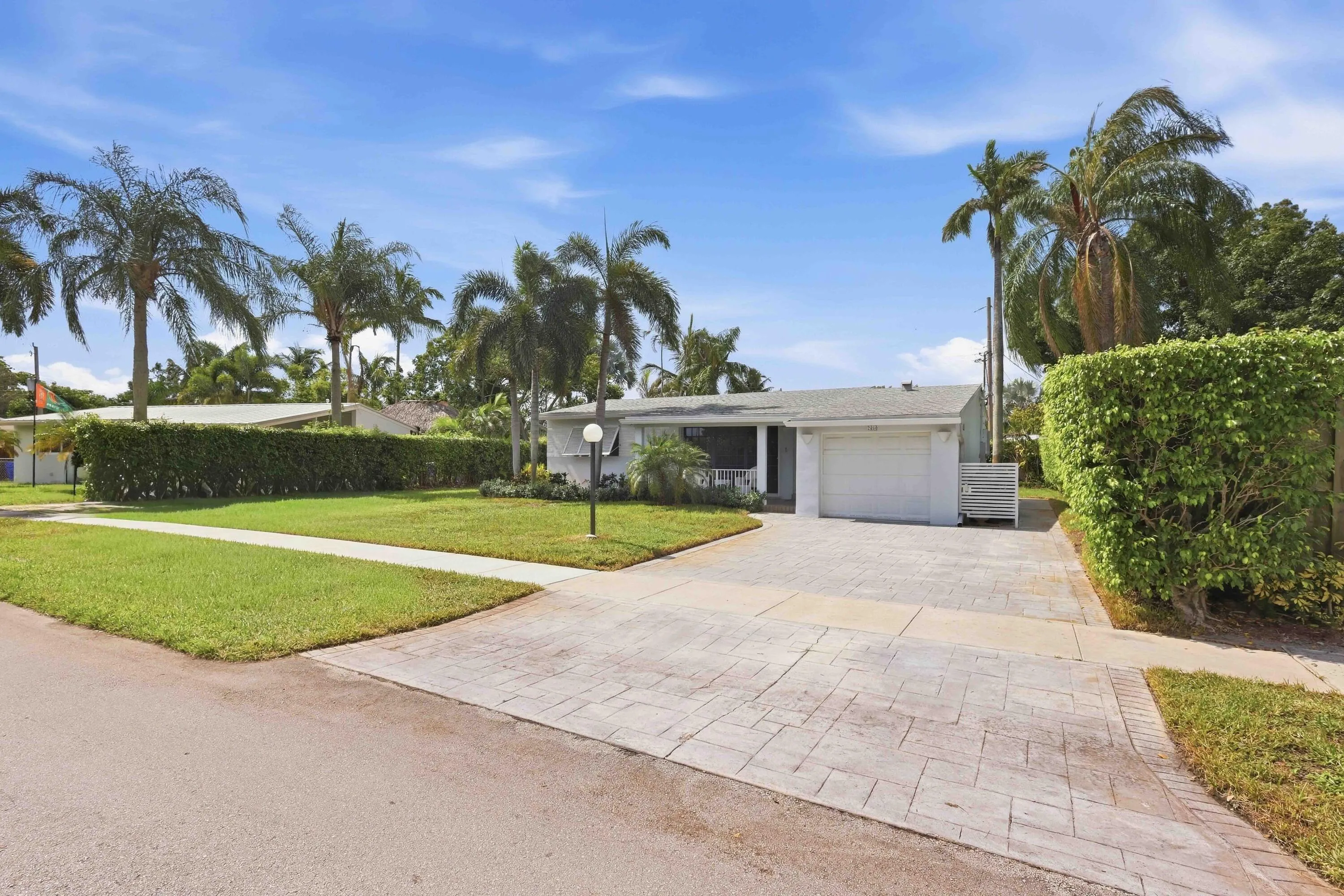 Single-story residence featuring a front lawn with mature palm trees, a stamped concrete driveway, and an attached garage