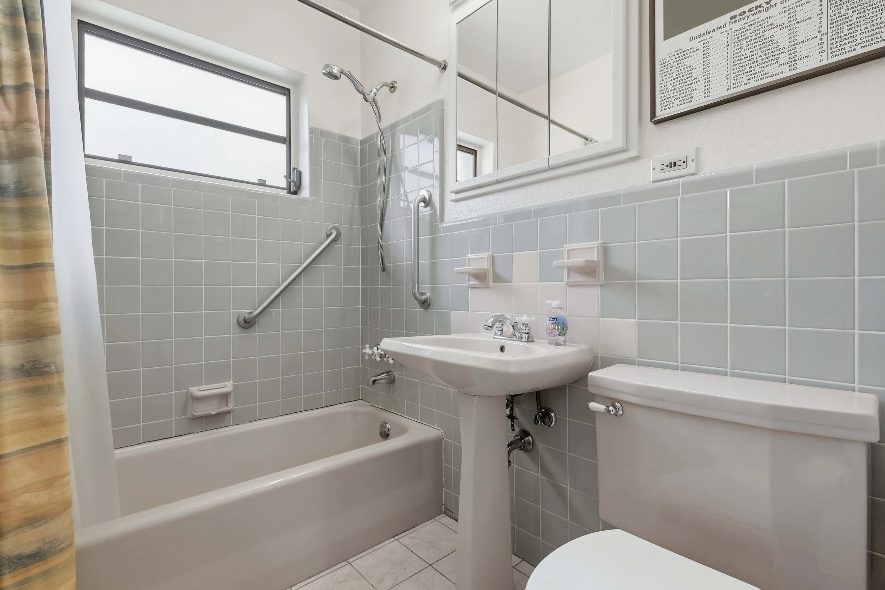 Bathroom featuring a pedestal sink, white ceramic toilet, bathtub with shower fixture, and a window