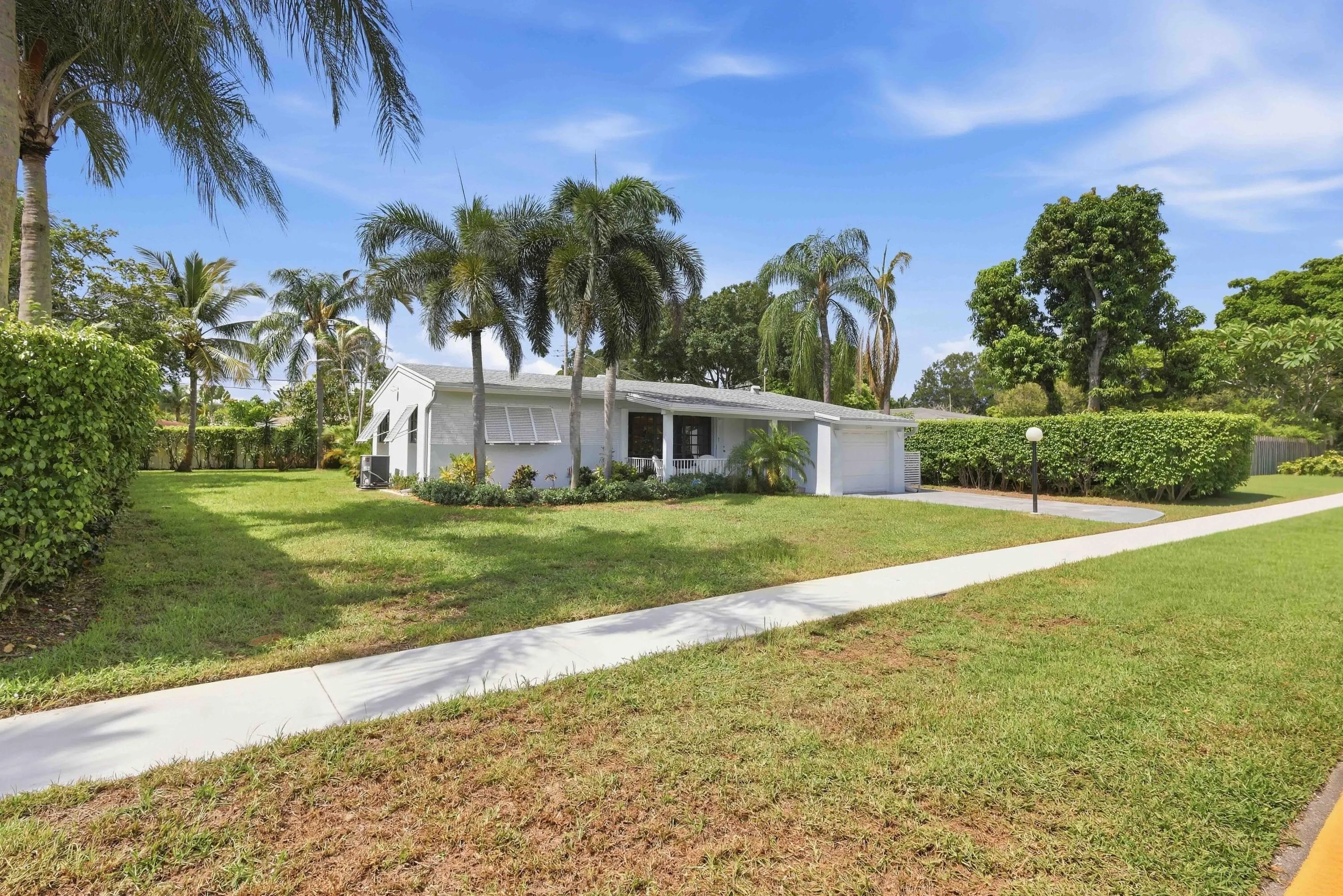 Single-story residence with a white exterior, attached garage, and mature palm trees