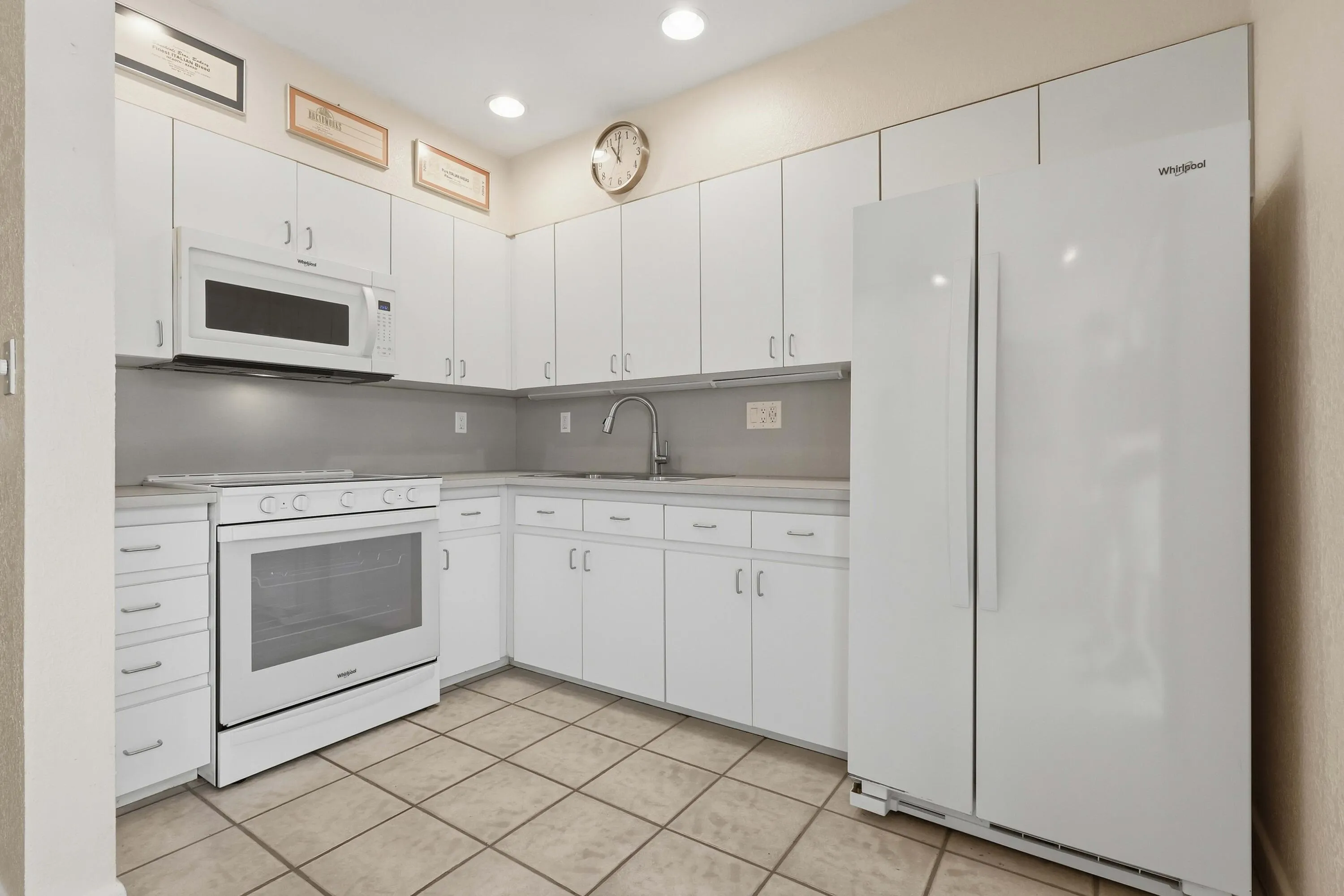 Kitchen featuring white cabinetry, light-toned countertops, tile flooring, and integrated white appliances