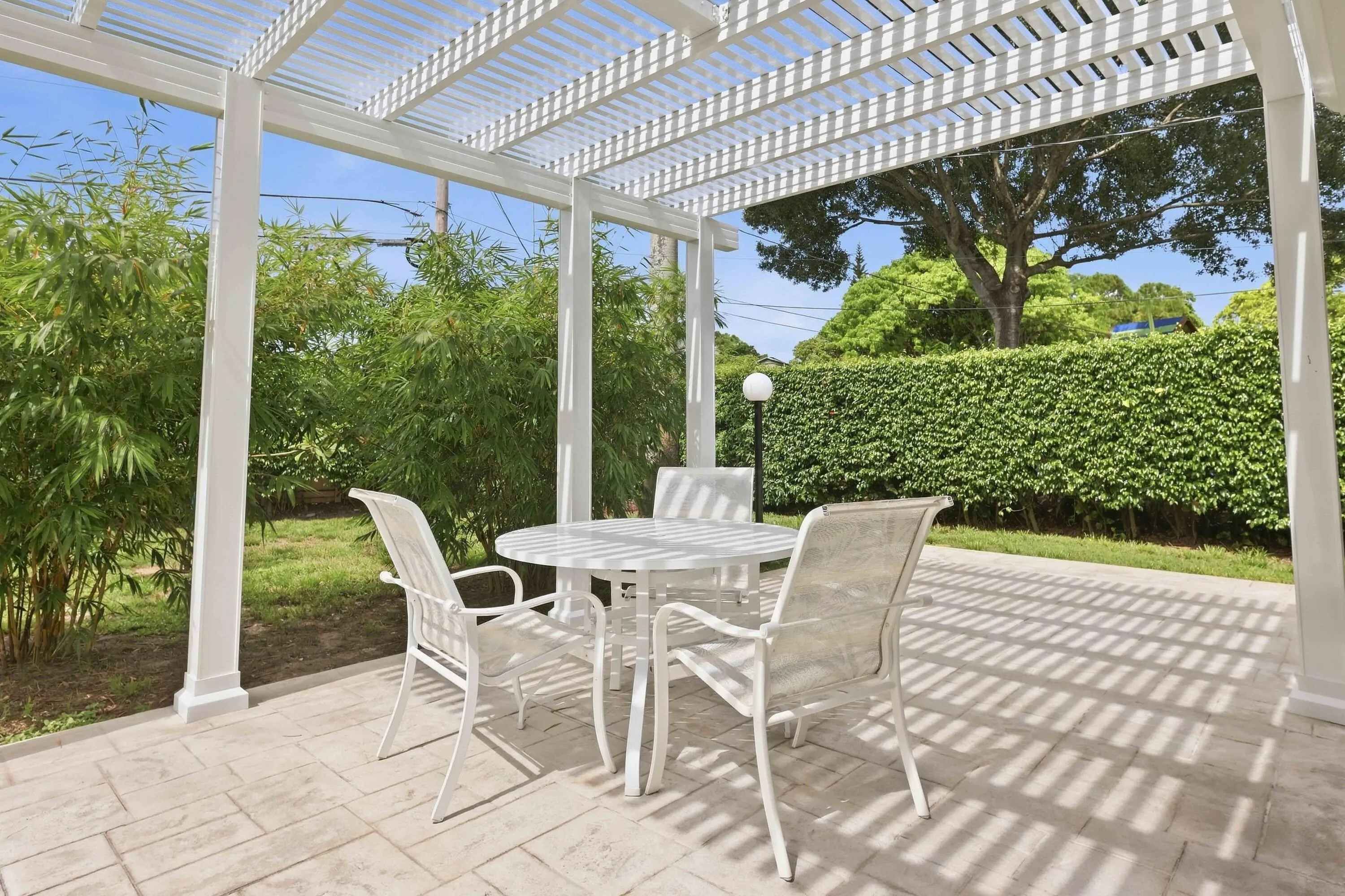 Expansive outdoor patio featuring a white pergola structure, stamped concrete flooring, and surrounding mature landscaping