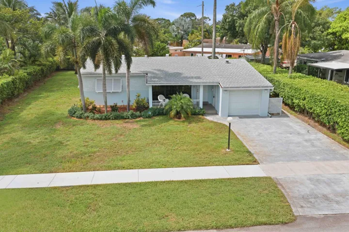 Single-story residence featuring a covered front porch, attached garage, concrete driveway, and established landscaping with palm trees