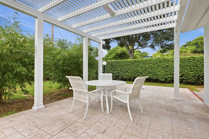 Expansive patio featuring a white pergola, stamped concrete flooring, and mature landscaping