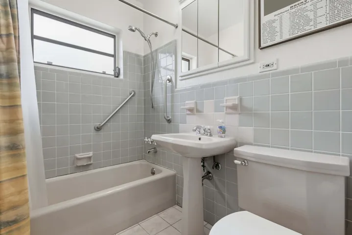 Bathroom featuring a pedestal sink, white ceramic toilet, bathtub with shower fixture, and a window