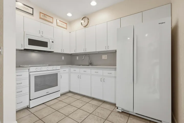 Kitchen featuring white cabinetry, light-toned countertops, tile flooring, and integrated white appliances