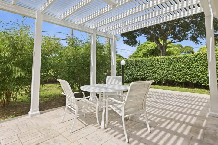 Expansive outdoor patio featuring a white pergola structure, stamped concrete flooring, and surrounding mature landscaping