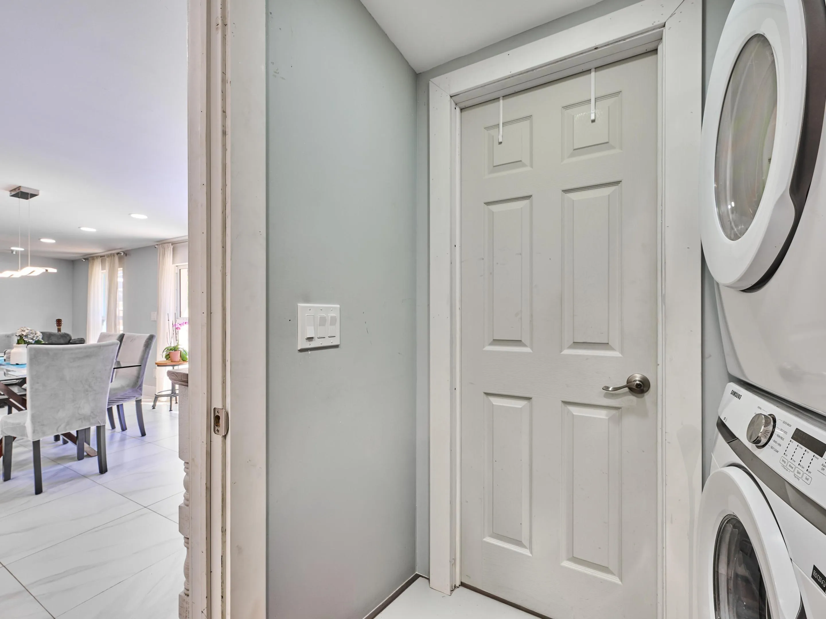 Laundry area with a stacked washer and dryer, adjacent to a room with tile flooring and recessed lighting