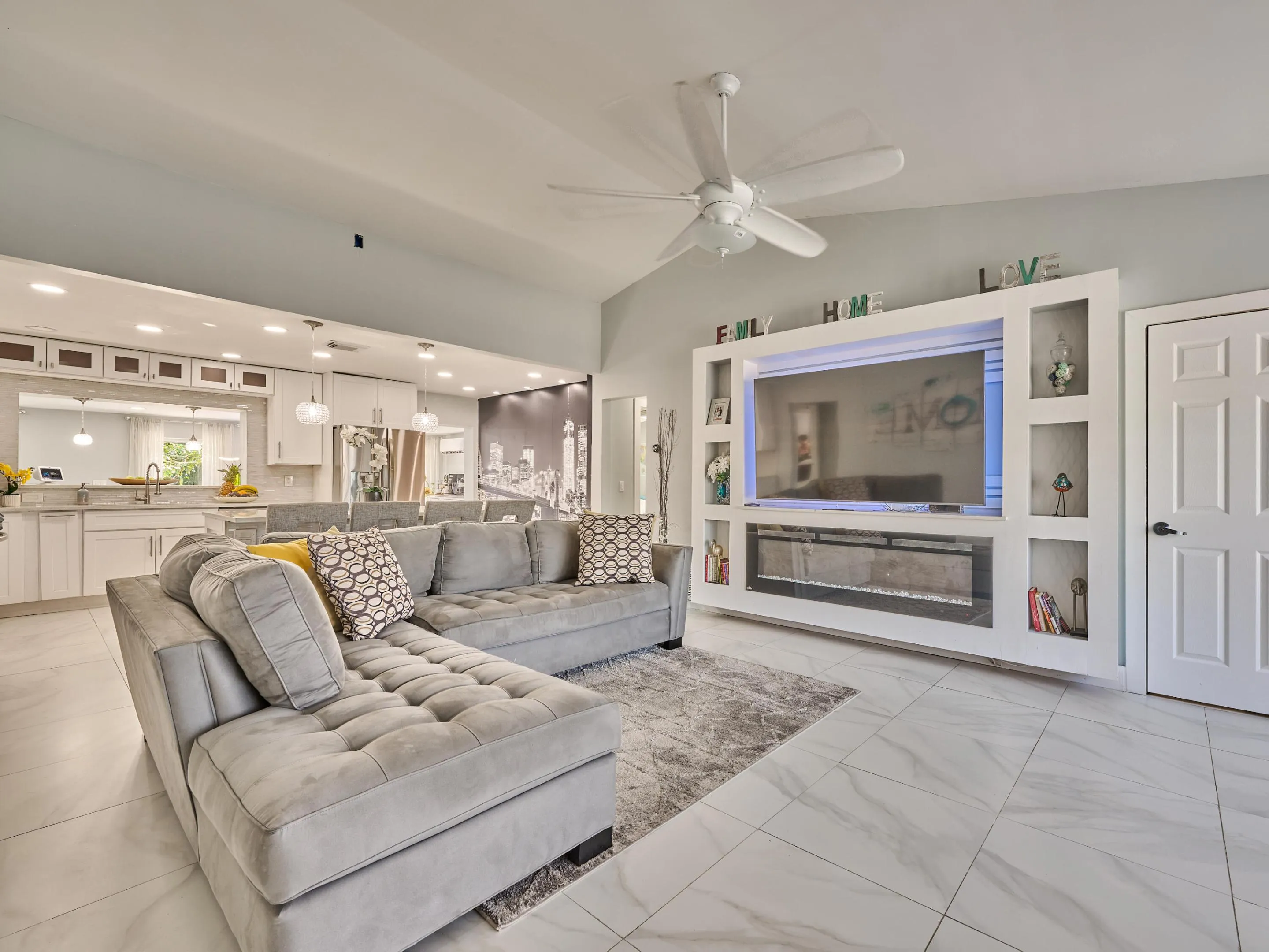 Open concept living area featuring large format tile flooring, a built-in media center with shelving, and a modern fireplace