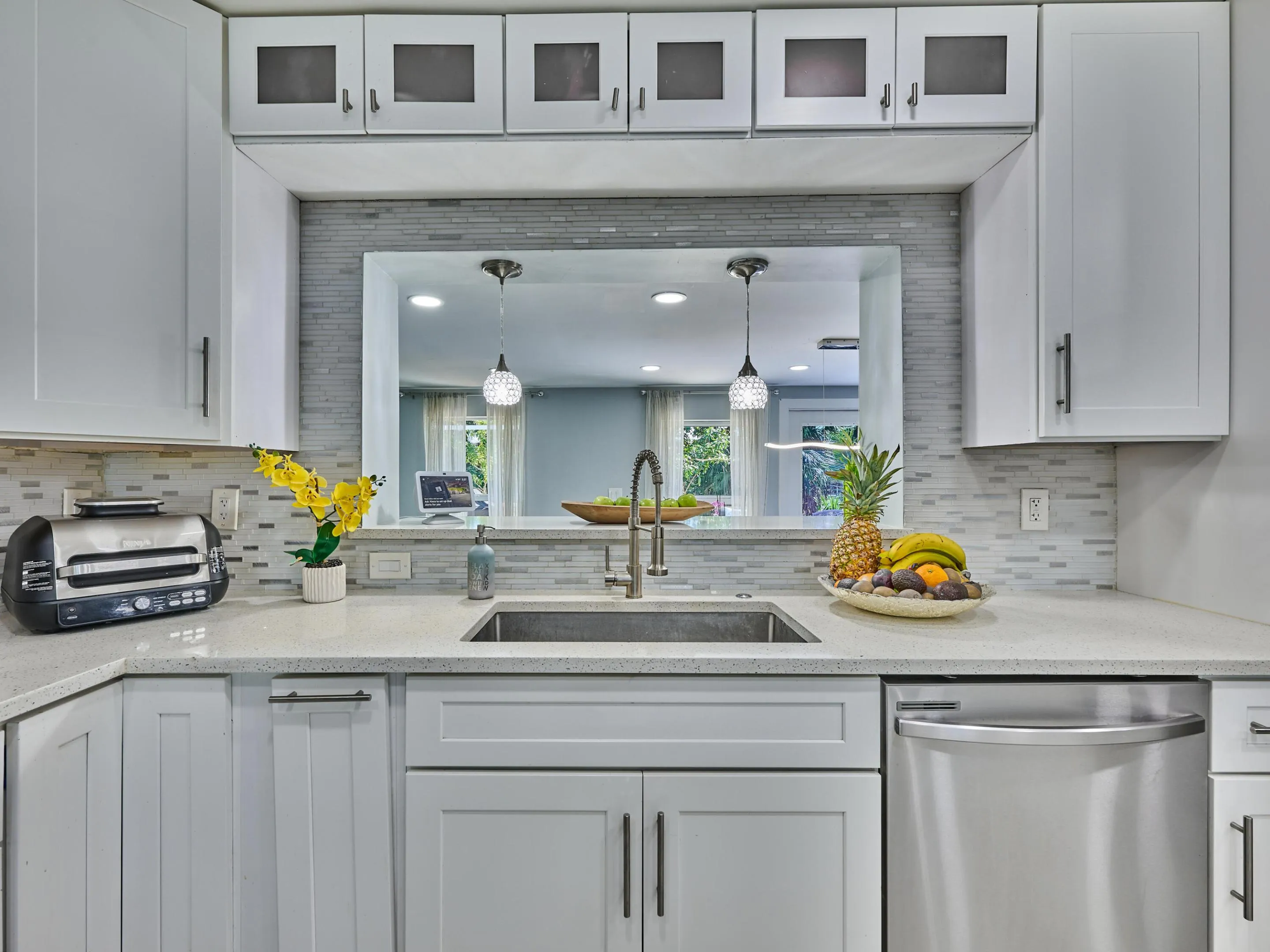 White shaker-style cabinetry with dark hardware, light speckled countertops, stainless steel sink with a gooseneck faucet, full tile backsplash, and a stainless steel dishwasher